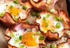 Baked ham and cheese egg cups served on a plate, garnished with herbs.